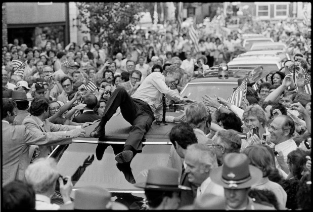 President Jimmy Carter leans across the roof of his car to shake hands along the parade route through Bardstown, Ky.