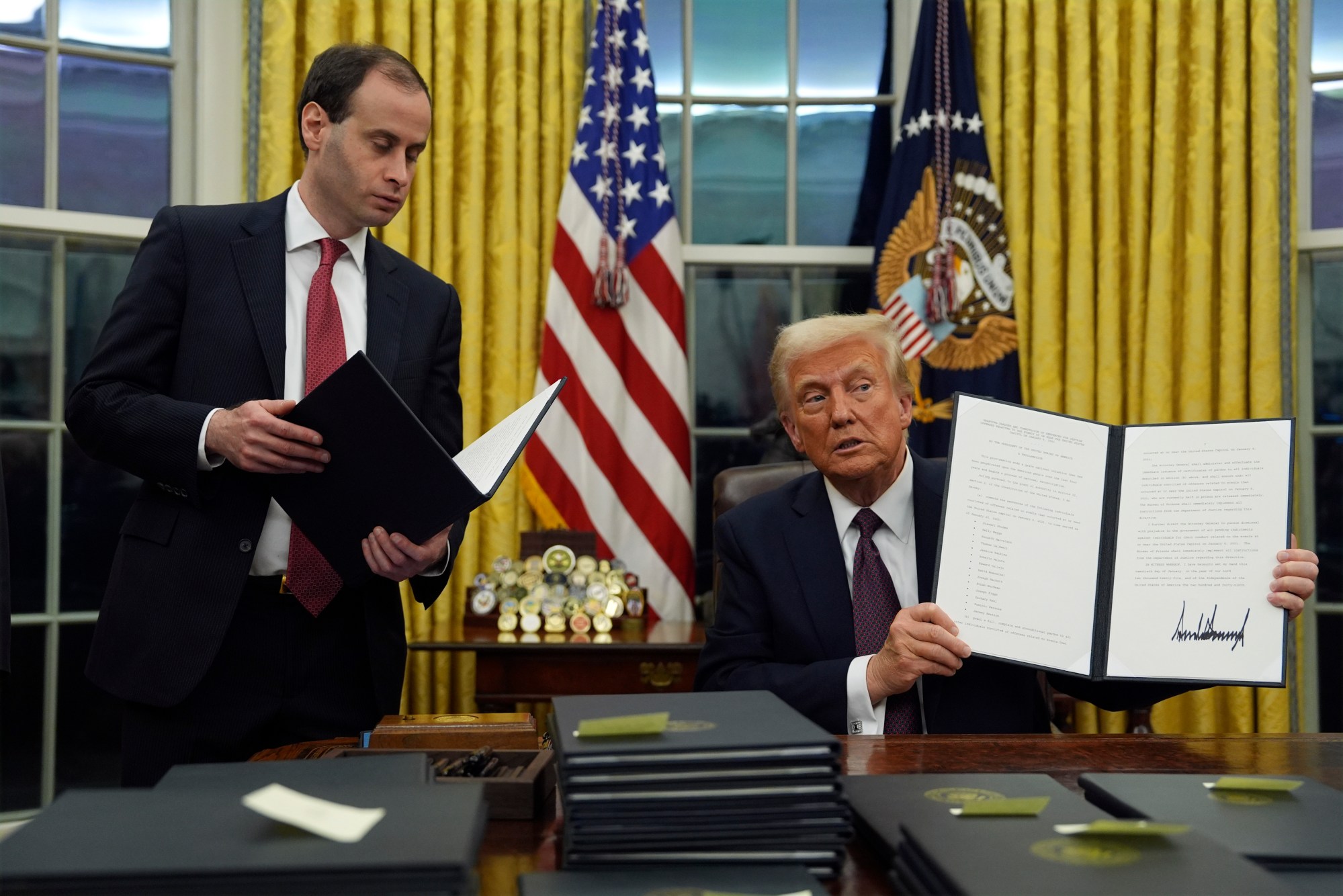 President Donald Trump holds up an executive order commuting sentences for people convicted of Jan. 6 offenses