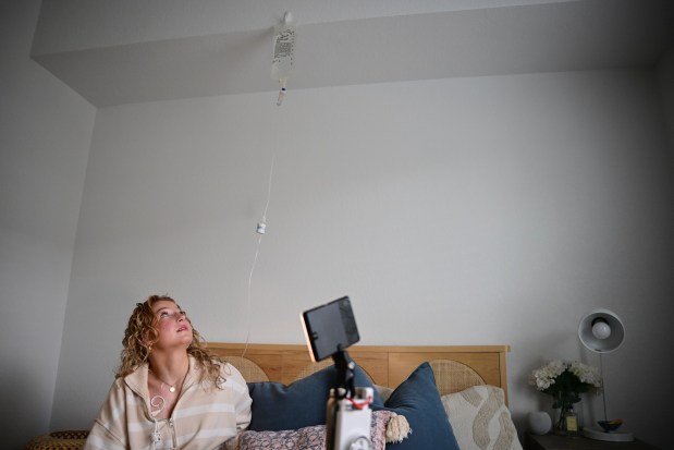 Lilly Downs, 20, hangs an IV bag high on the wall above her before filming a video for TikTok at her apartment in Fort Collins, Colorado on Thursday, Oct. 17, 2024. (Photo by Hyoung Chang/The Denver Post)